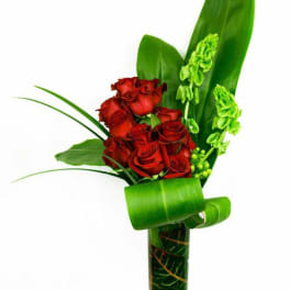 Red roses arranged with green leaves in a tall glass vase