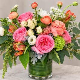 Mixed pink, peach, and white flowers arranged in a glass vase