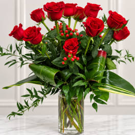 Red roses arranged in a clear glass vase with glossy greenery
