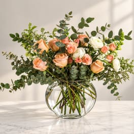 Peach and white roses in a clear glass vase with airy greenery