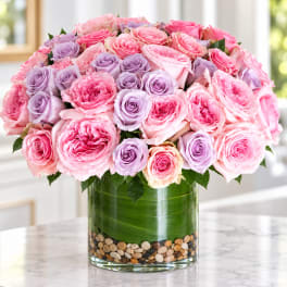 Pink and lavender roses arranged in a clear glass vase with pebbles