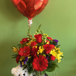 Red heart balloon above a mixed flower arrangement with a teddy bear