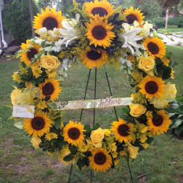 Sunflower and yellow rose wreath on a stand with a ribbon banner