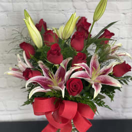 Bouquet of red roses and pink lilies in a glass vase with a red ribbon
