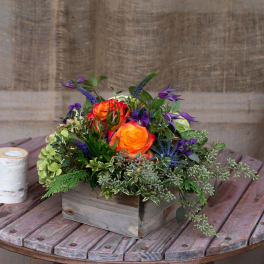 Orange roses in a wooden box with purple flowers and greenery