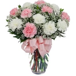 Pink and white carnations in a clear glass vase with a pink ribbon