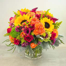 Bright mixed bouquet with sunflowers, roses, and calla lilies in a glass vase