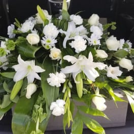 White floral casket spray with lilies, roses, and carnations