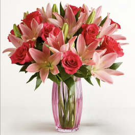 Pink lilies and red roses arranged in a tall glass vase