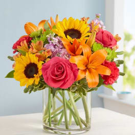 Bright mixed bouquet with sunflowers, roses, lilies, and carnations in a clear glass vase