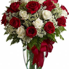 Red and white roses in a glass vase with a red ribbon