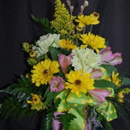 Yellow and pink mixed flower arrangement in a pink container with ribbon