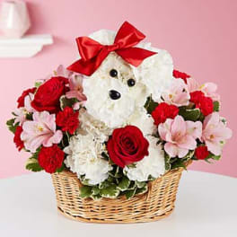White teddy bear with a red bow in a basket of red and pink flowers