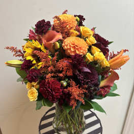 Bouquet of orange, yellow, and burgundy flowers in a clear glass vase