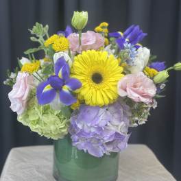 Mixed bouquet in a green glass vase with yellow, purple, pink, and white blooms