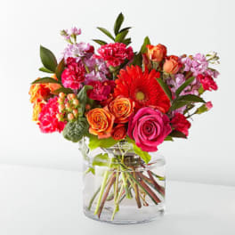 Mixed bouquet of roses, gerbera daisies, and carnations in a clear glass vase
