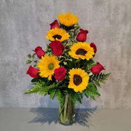 Bouquet of red roses and yellow sunflowers in a clear glass vase