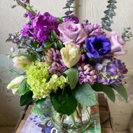 Mixed bouquet of purple, pink, and green flowers in a glass vase