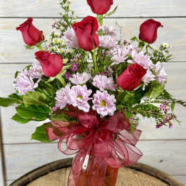 Red roses and pale pink daisies in an amber vase with a red ribbon