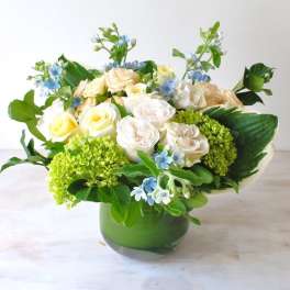 Bouquet of cream roses and blue flowers in a green glass vase