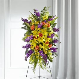 Tall standing floral spray with yellow lilies, orange roses, and purple flowers