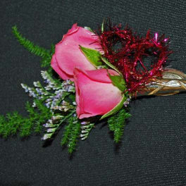 Pink rose boutonniere with red tinsel and greenery on a black background