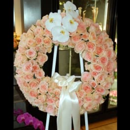 Heart-shaped wreath of pale pink roses with white orchids and a satin ribbon