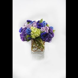 Purple and blue flower arrangement in a clear square vase
