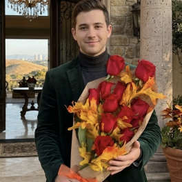 Man holding a bouquet of red roses wrapped in paper with autumn leaves