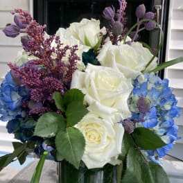 White roses and blue hydrangeas in a glass vase with purple accents