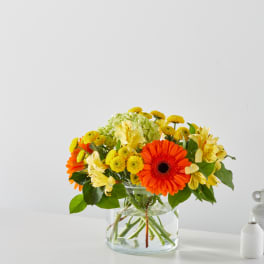 Orange gerbera daisies and yellow flowers in a clear glass vase