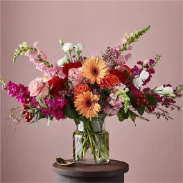 Mixed bouquet of pink, red, white, and peach flowers in a clear glass vase