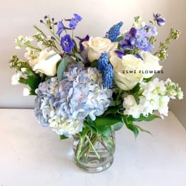 Bouquet of white roses, blue hydrangeas, and purple flowers in a glass vase