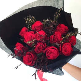 Bouquet of red roses wrapped in black paper with a pink ribbon
