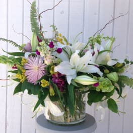 Mixed bouquet of white lilies, pink flowers, and green blooms in a glass vase