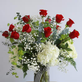 Red roses and white hydrangeas in a glass vase with a striped ribbon