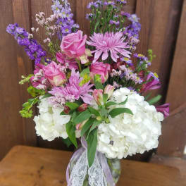 Pink roses and purple flowers arranged in a glass vase with white hydrangeas
