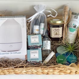 Gift basket with an essential oil diffuser, candles, bath items, and a small air plant