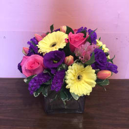 Pink roses and yellow gerbera daisies in a square glass vase