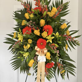 Large standing floral spray with red gerberas, yellow roses, and lilies