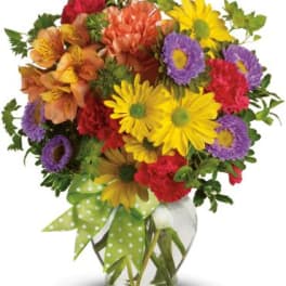 Bright mixed bouquet of daisies, asters, and carnations in a glass vase with a green polka-dot bow