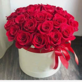 Round box of red roses topped with a red satin ribbon bow