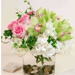 Pink roses and white hydrangeas in a clear glass vase with green orchids