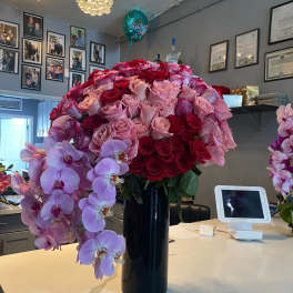 Tall arrangement of red and pink roses with cascading pink orchids in a black vase