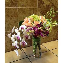 Orchid arrangement in a clear glass vase with peach and white blooms