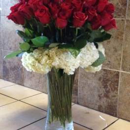 Tall vase arrangement of red roses with white hydrangeas