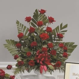 Tall arrangement of red roses with a red ribbon on a white pedestal