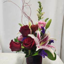 Red roses and pink lilies in a square glass vase with heart picks