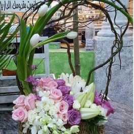 Basket arrangement of pink and purple roses with white lilies and arching branches