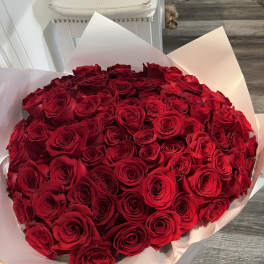 Large round bouquet of tightly packed red roses wrapped in white paper